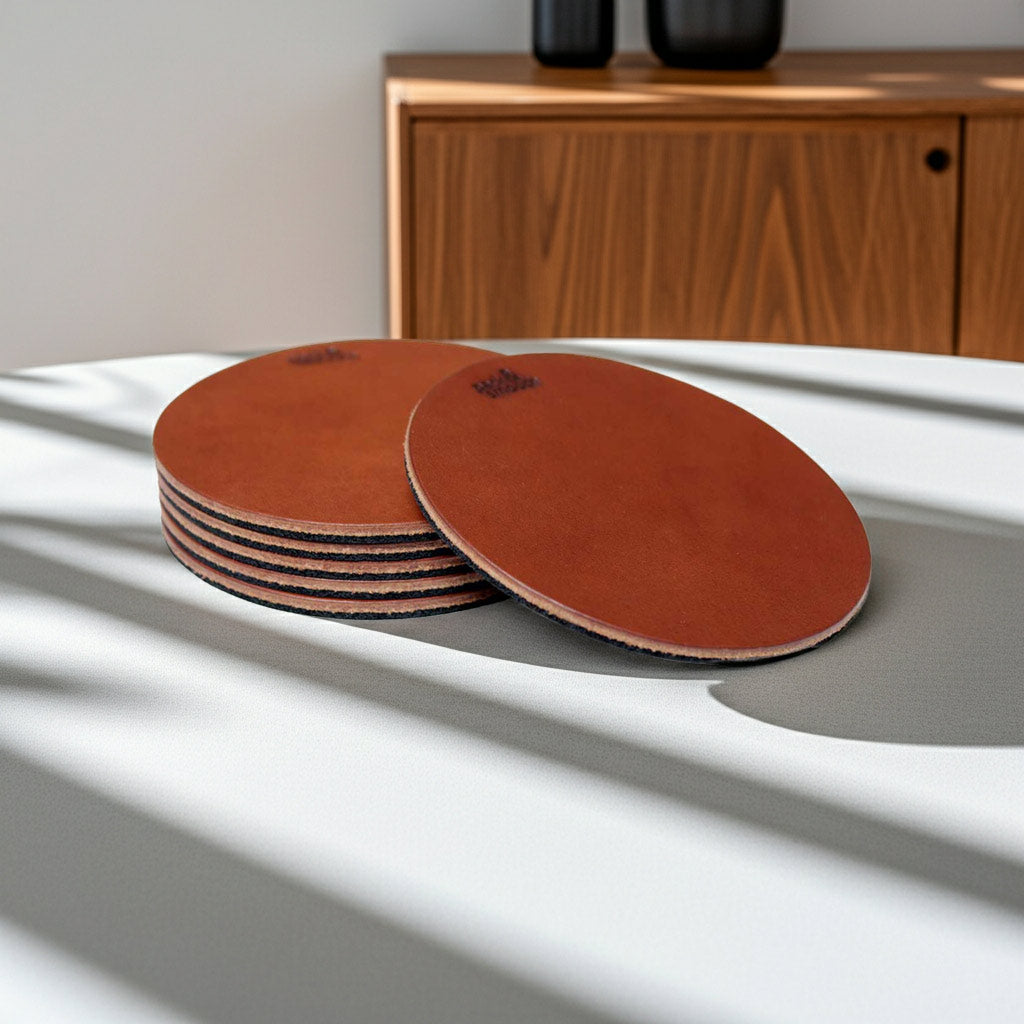Hellbraune Glasuntersetzer aus Leder auf einer weißen Fläche im Sonnenlicht, Sideboard im Hintergrund, Modell DEXTER