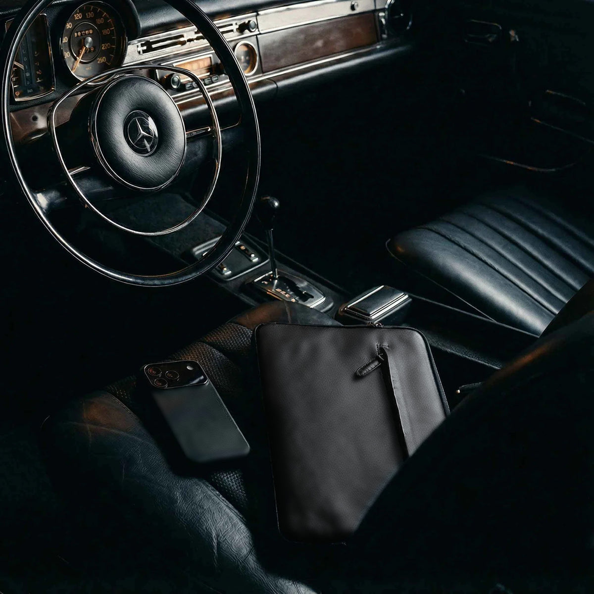 Schwarze MacBook Hülle auf dem Ledersitz eines Oldtimers neben einem Smartphone, Modell ANGUS