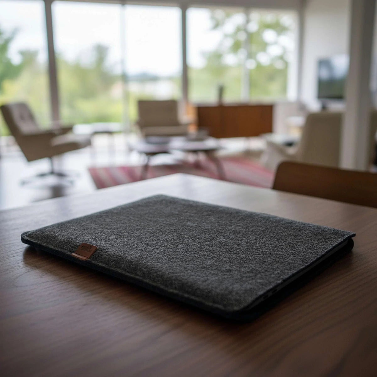 Anthrazitfarbene MacBook Hülle aus Merino-Wollfilz liegend auf einem Nussbaumtisch in einem hellen Raum, Modell SUFFOLK