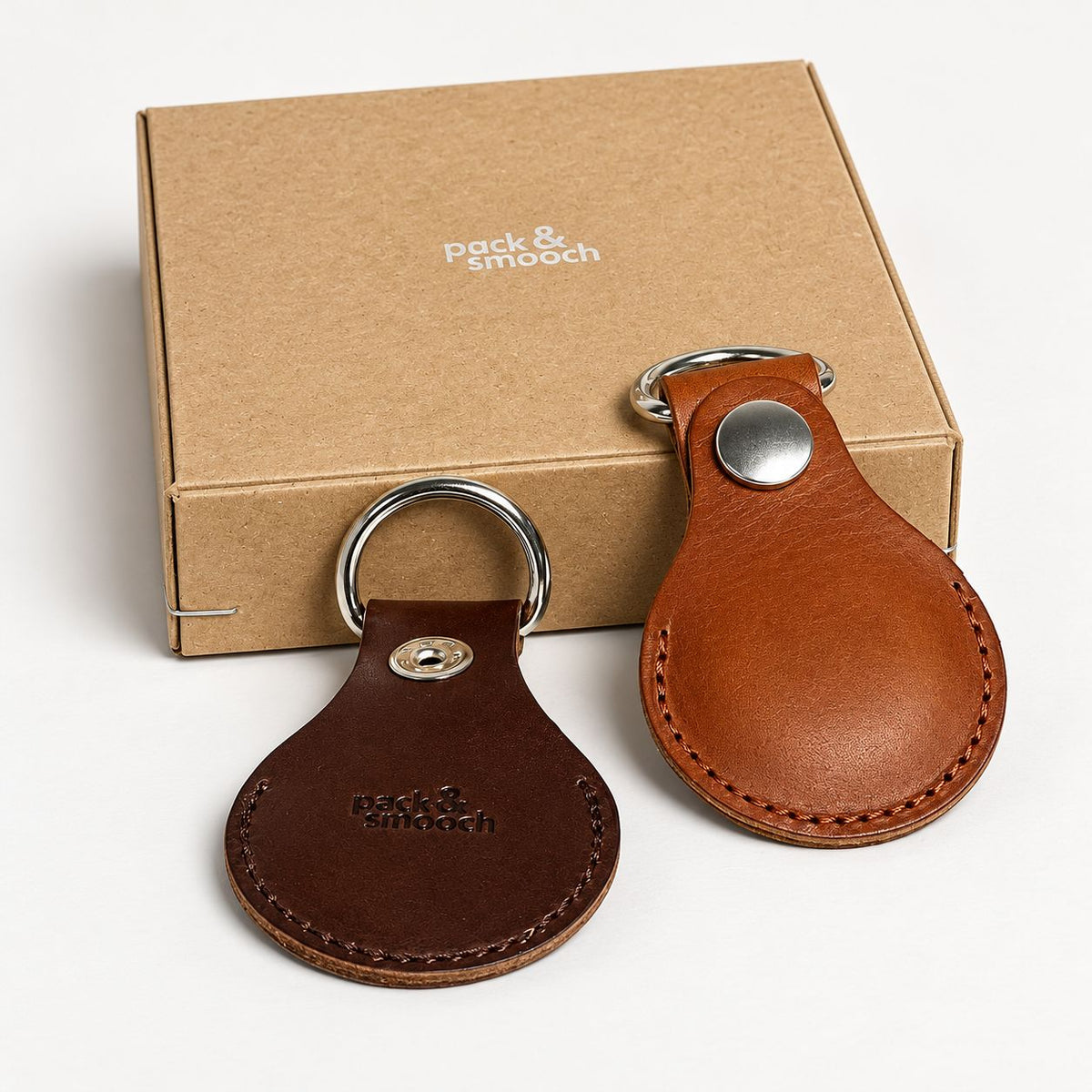 Zwei AirTag Schutzhüllen aus Leder vor der Geschenkschachtel aus Karton