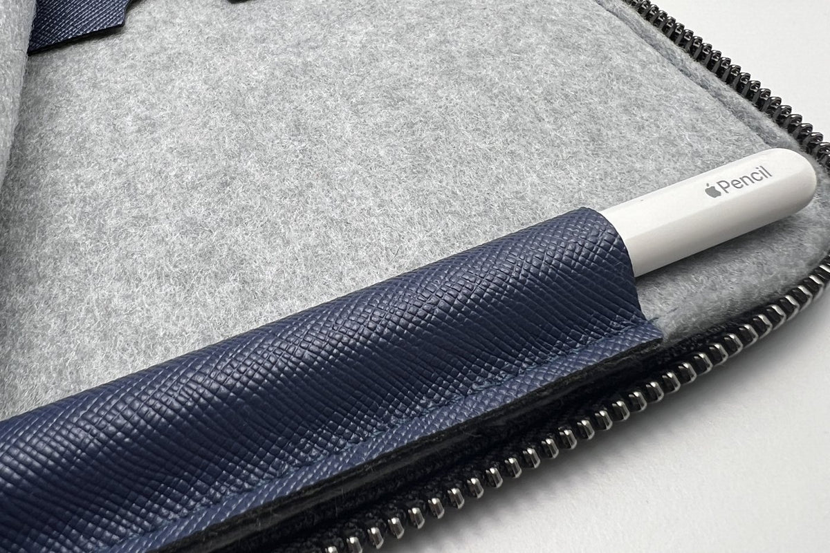 Der Apple Pencil steckt in seiner aufgenaehten Lasche aus koenigsblauem Oleatex am Rand der veganen iPad-Huelle ANGUS, daneben hellgrauer Violan-Filz und der umlaufende Reissverschluss